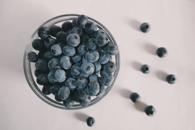 Blauwe bessen in een glazen pot op een witte ondergrond.