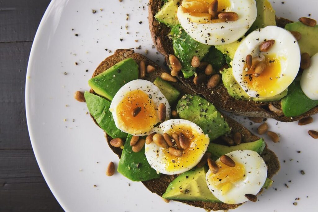 Een bord met brood met avocado, ei en pijnboompitten.