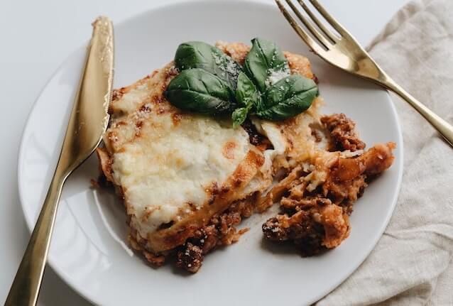 Een stuk koolhydraatarme ovenschotel van aubergine en gehakt op een wit bord met bestek.