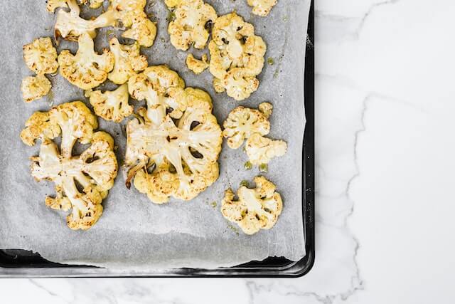 Een paar bloemkoolstronken op een bakplaat voor de koolhydraatarme ovenschotel