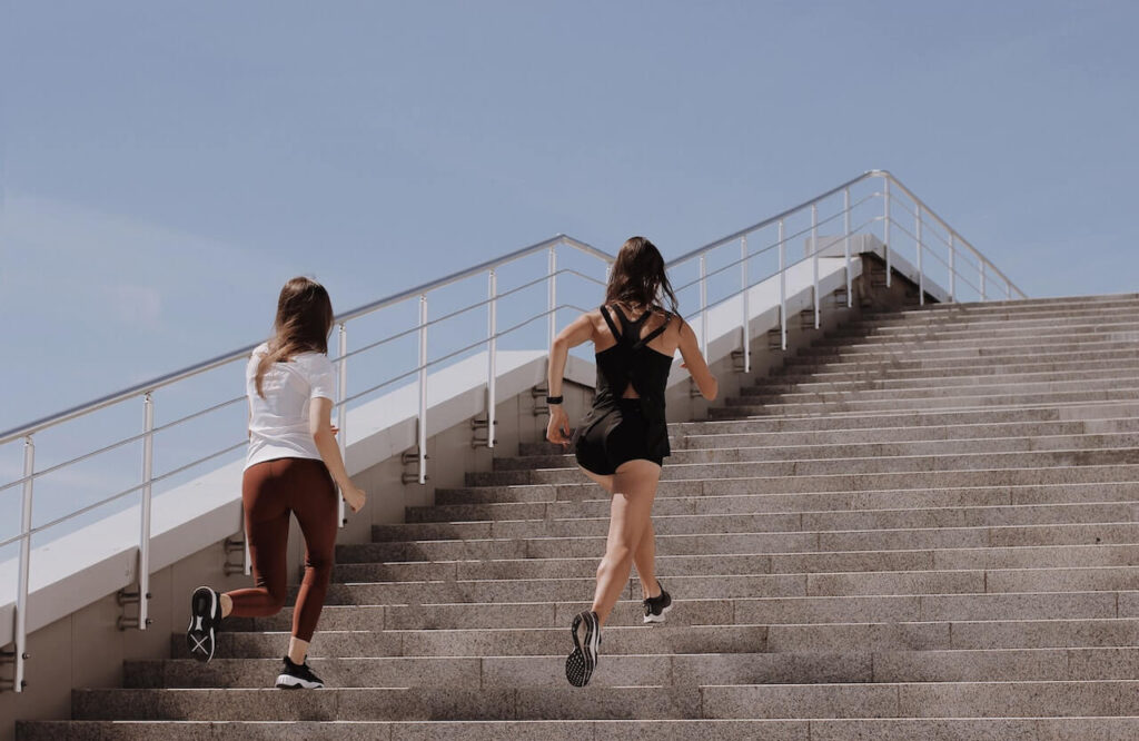 Twee vrouwen aan het rennen naar boven op een trap met mooi weer.