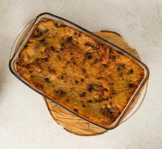 De koolhydraatarme ovenschotel van pompoen-spaghetti in een schaal op een houten onderzetter.