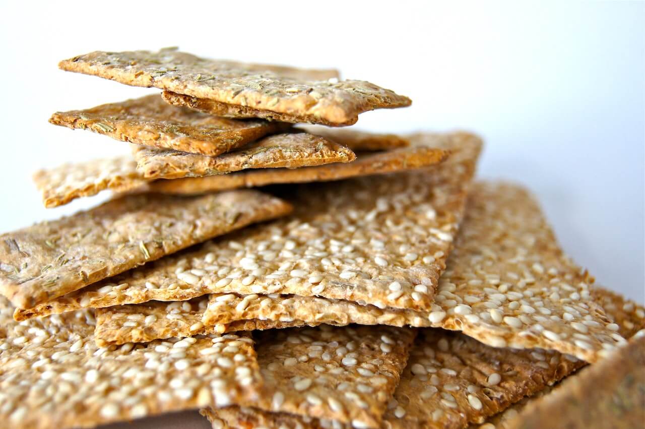 Koolhydraatarme crackers met sesamzaadjes op een stapel met een witte achtergrond.