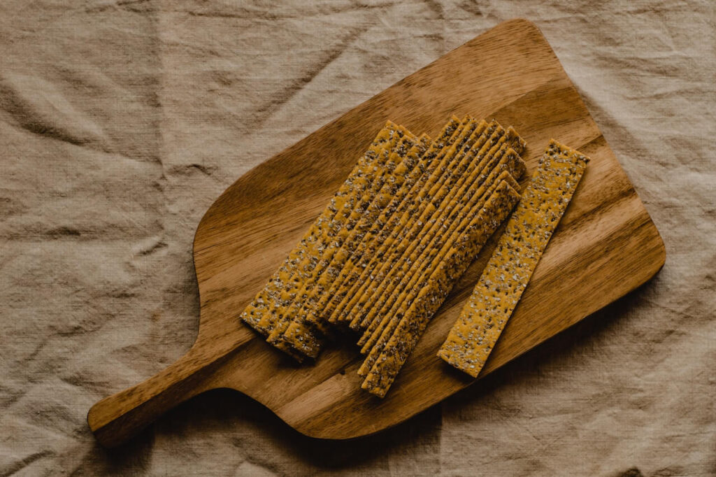 Koolhydraatarme crackers met rozemarijn en zeezout op een houten plank op een bruin tafelkleed.